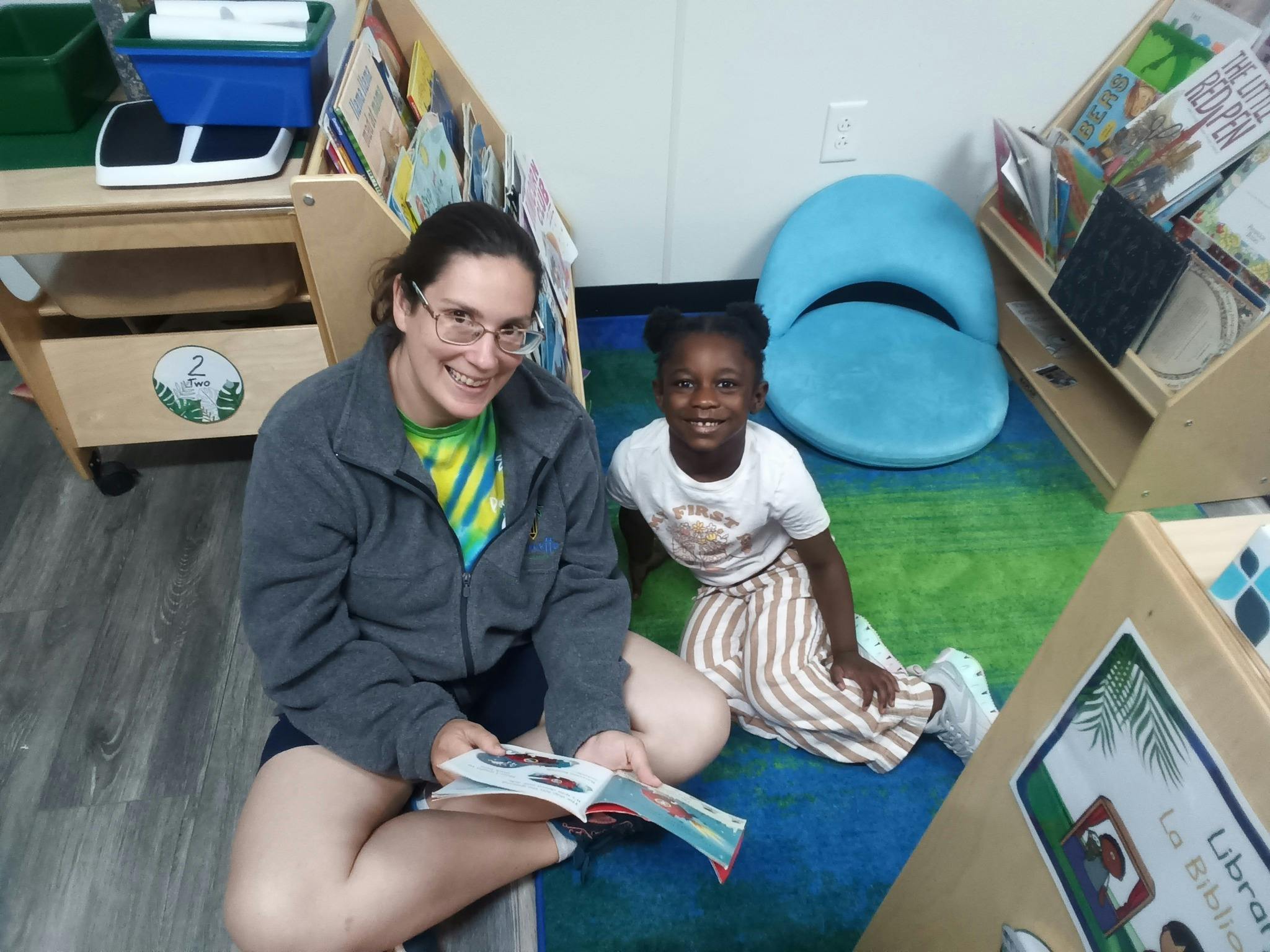 Adult and child sitting on floor reading a book in a classroom