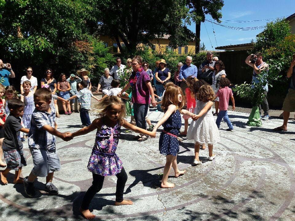 Children holding hands in a circle with adults watching in the background