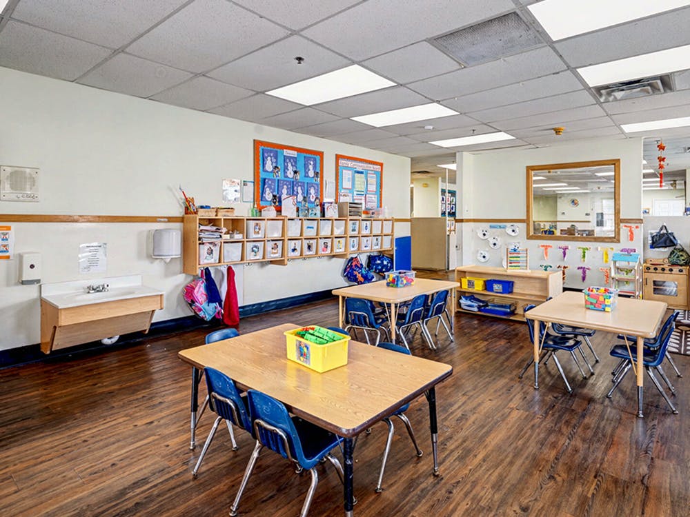 Empty classroom with small tables and chairs, wall decorations, and a sink