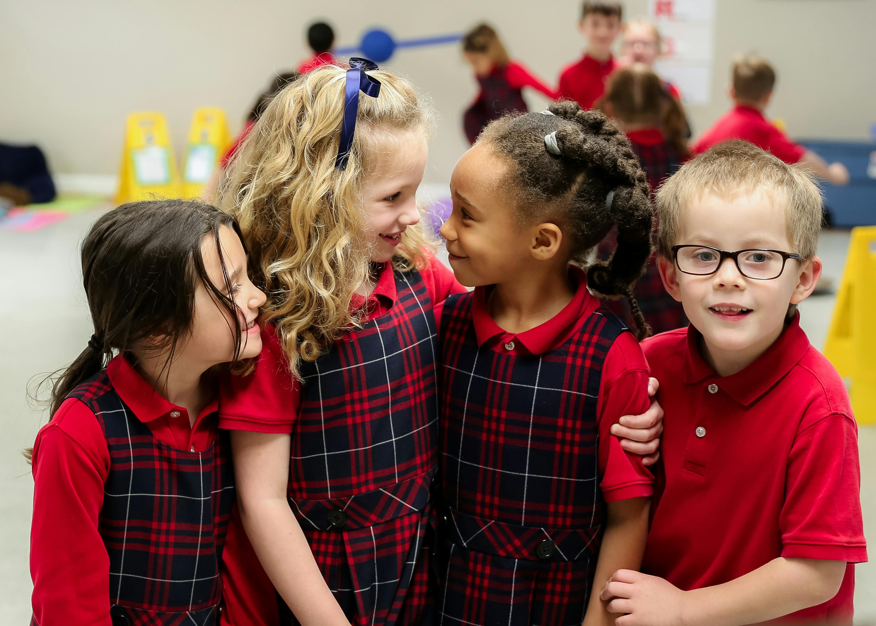 Four children in plaid uniforms interacting in a classroom
