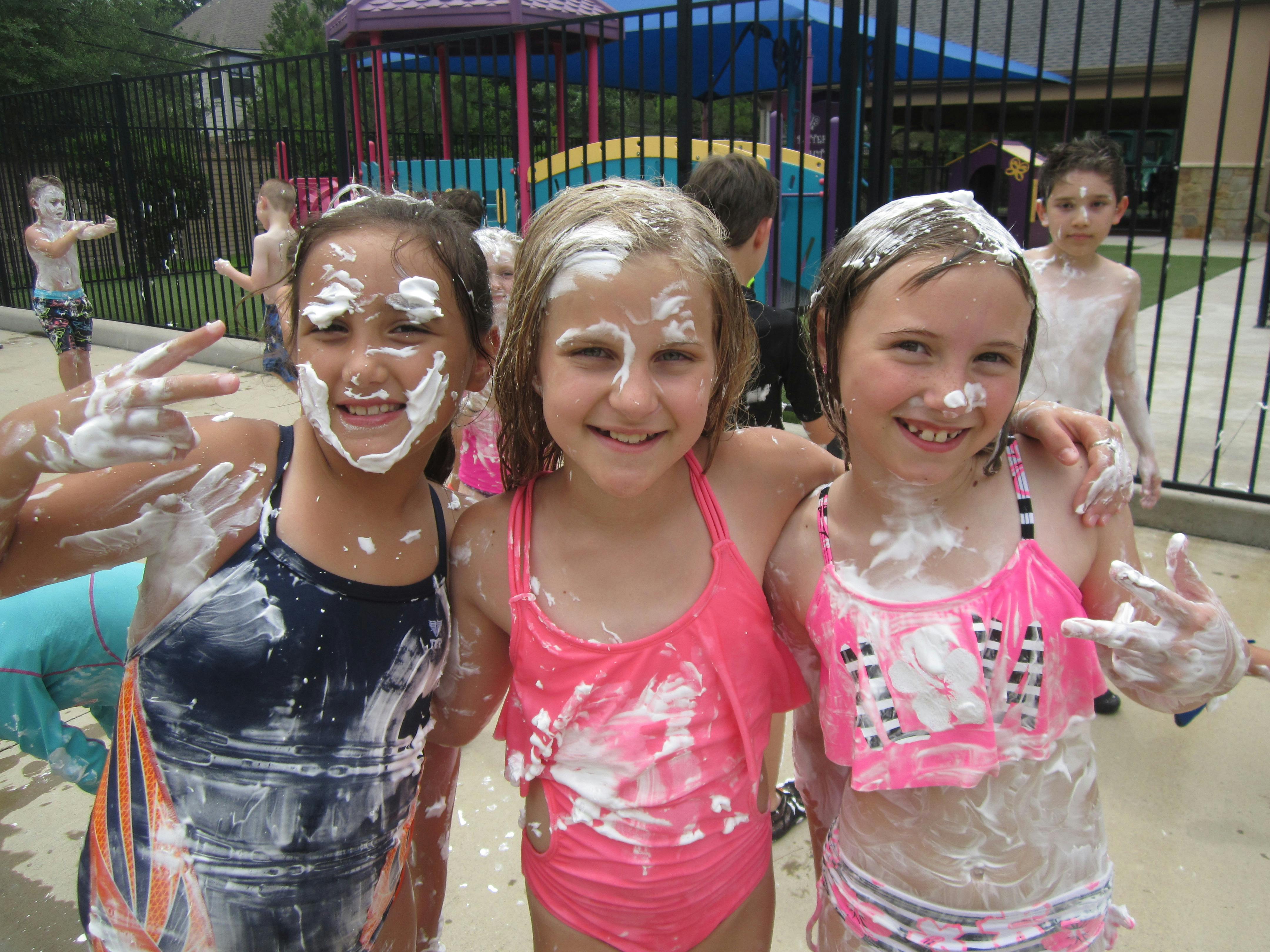 Three children covered in white foam, smiling
