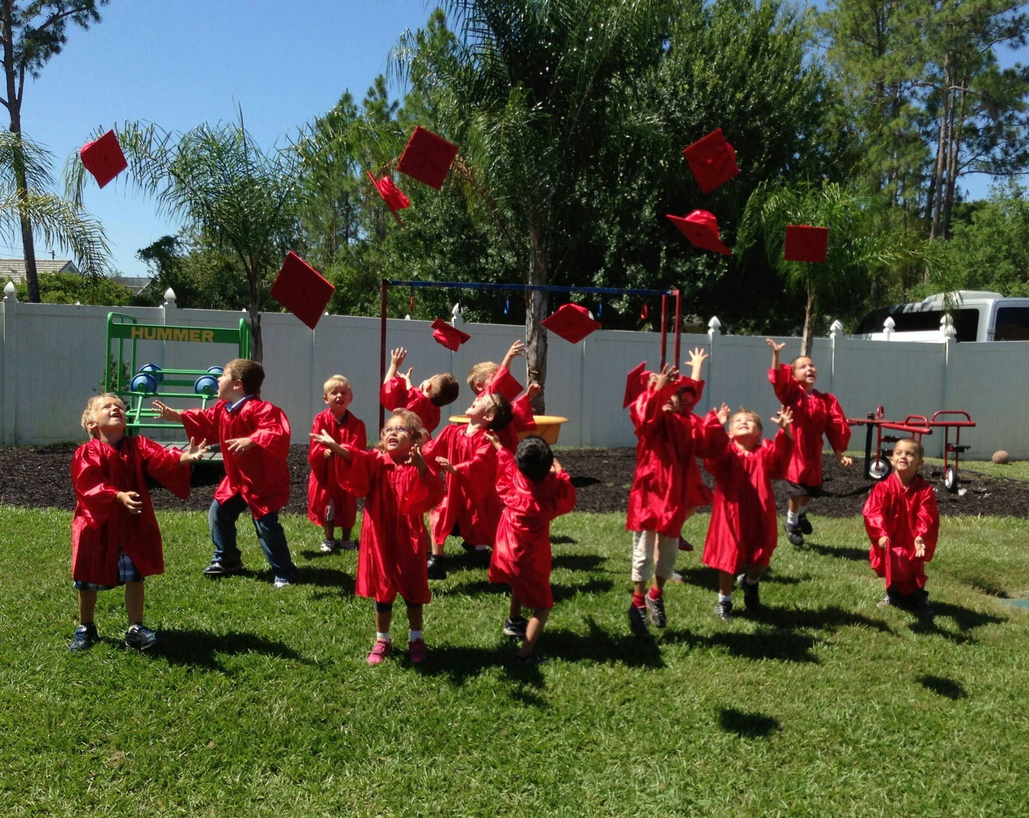 Children in red graduation gowns throwing caps in the air outdoors