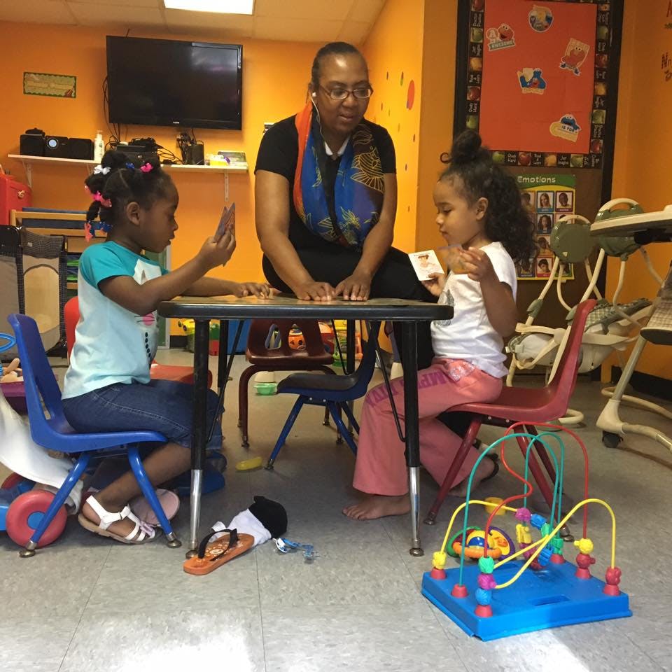 Adult and two children sitting at a table in a classroom
