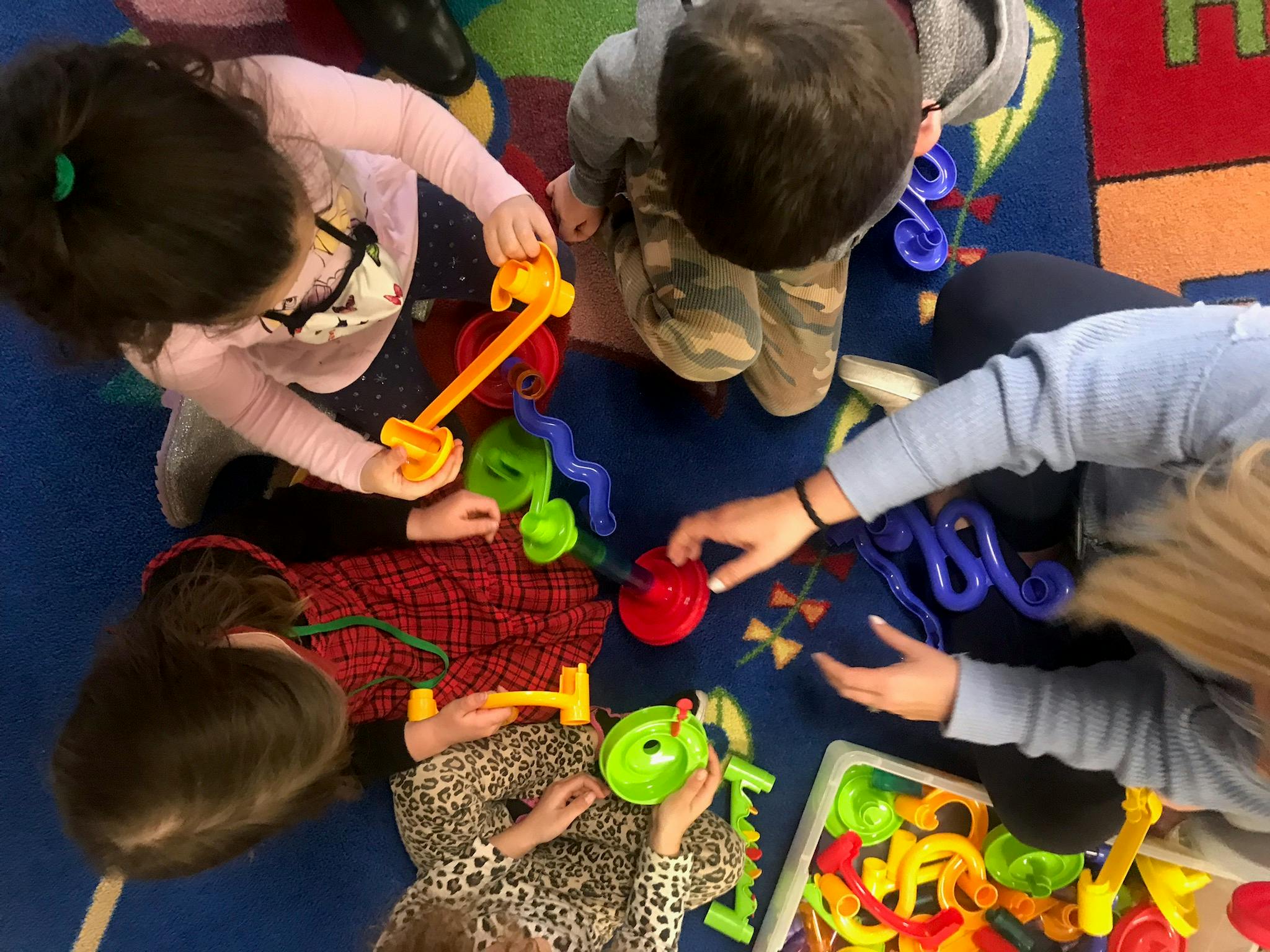 Children and an adult playing with colorful toys on a rug