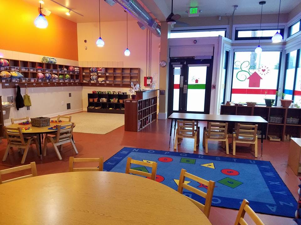 Empty classroom with small tables and chairs, cubbies, and a play rug