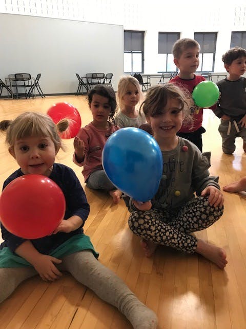 Children sitting on a wooden floor holding balloons