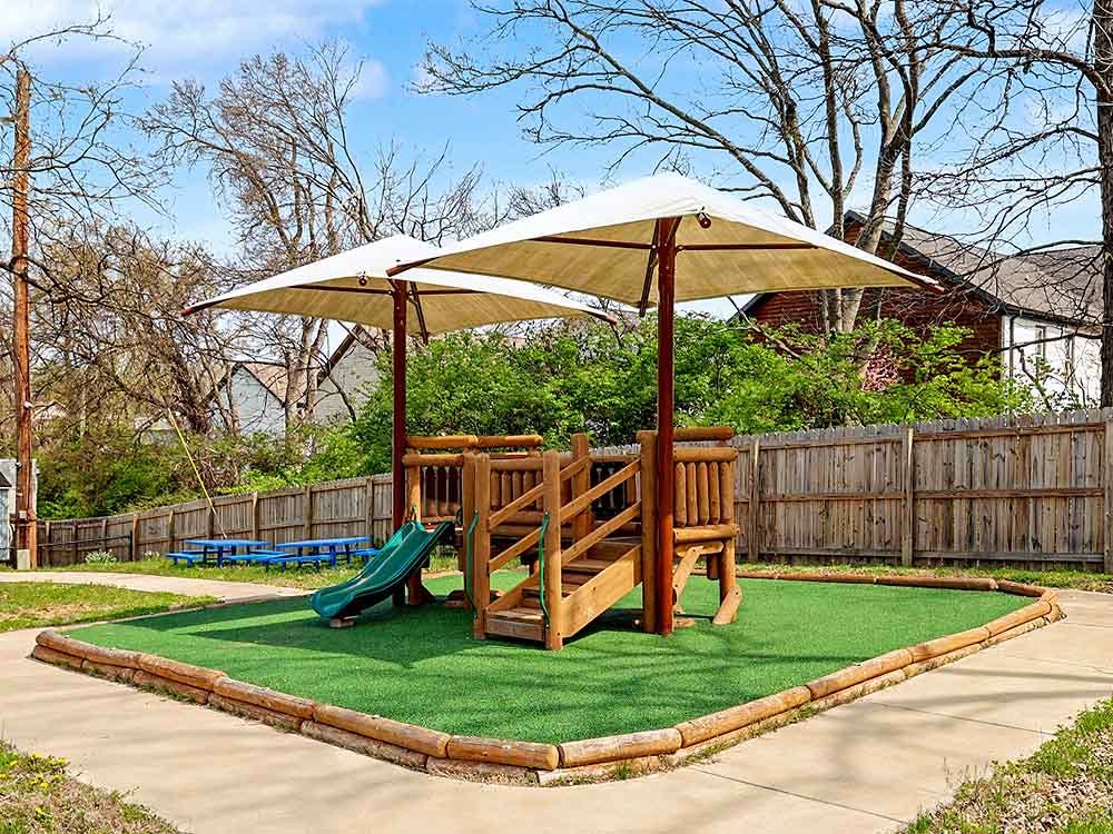 Wooden playground with a green slide and two large white umbrellas providing shade