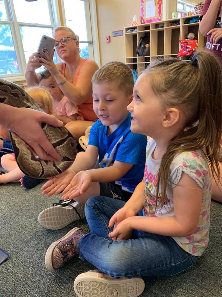Children sitting on floor looking at a snake held by a person