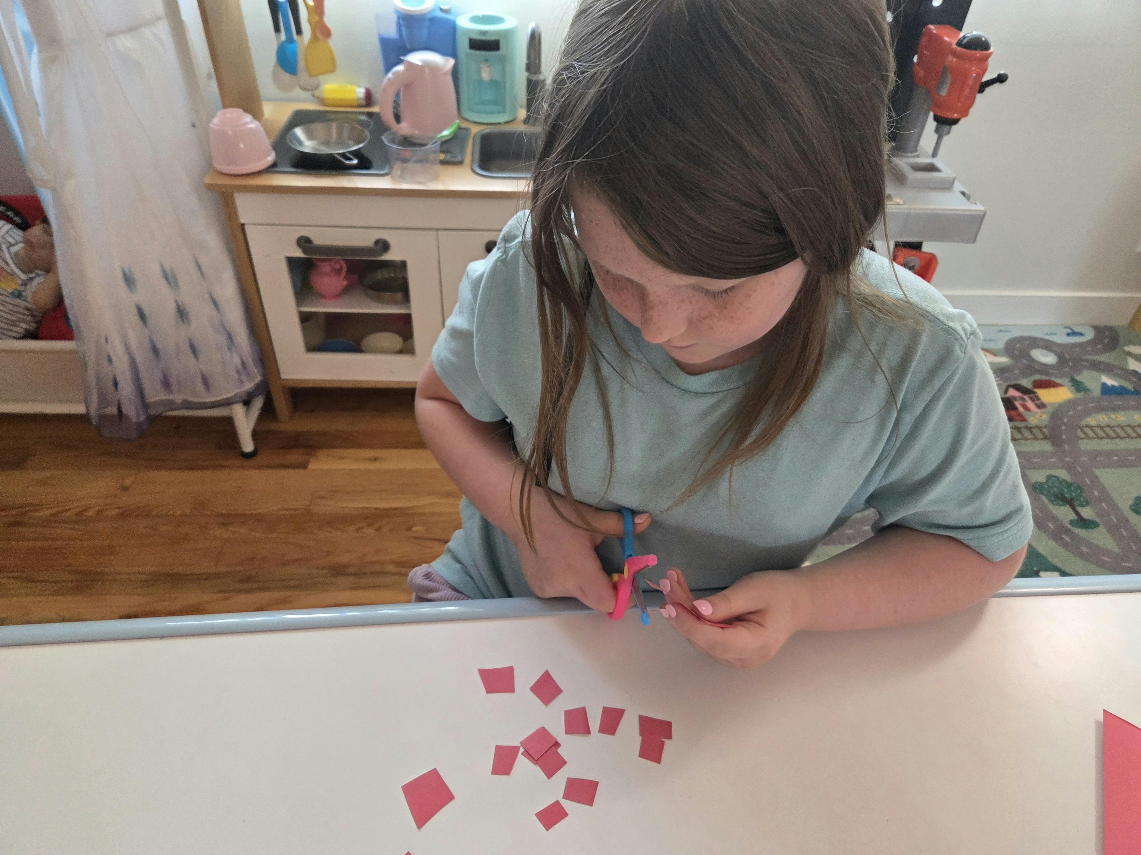 Child cutting small paper squares with scissors at a table