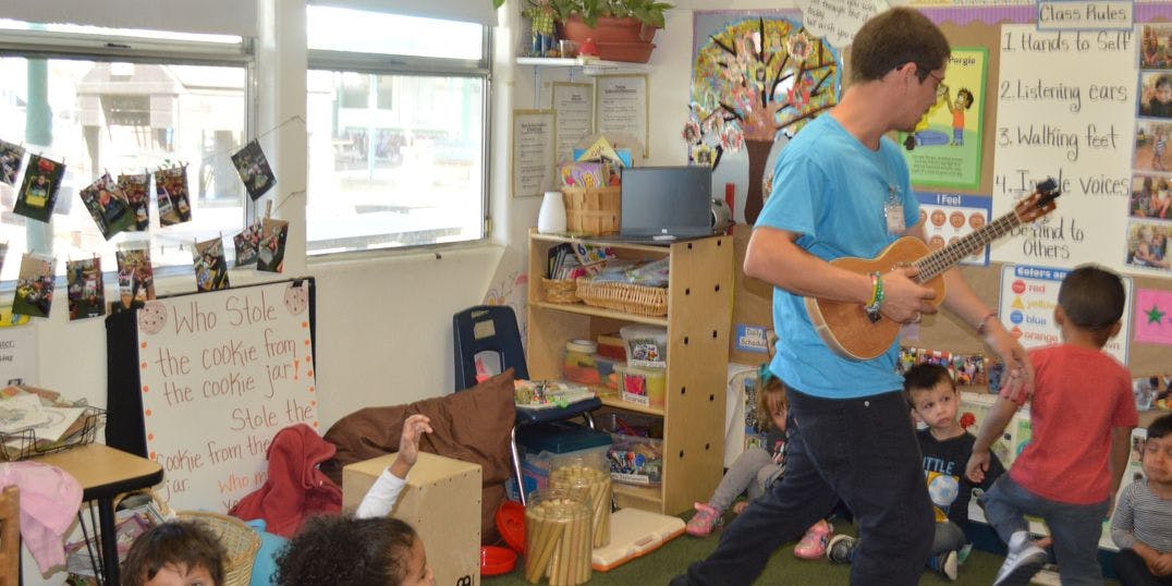 Person playing ukulele for children in a classroom