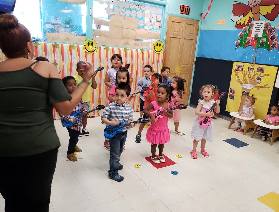 Adult leading a group of children playing with toy guitars in a classroom