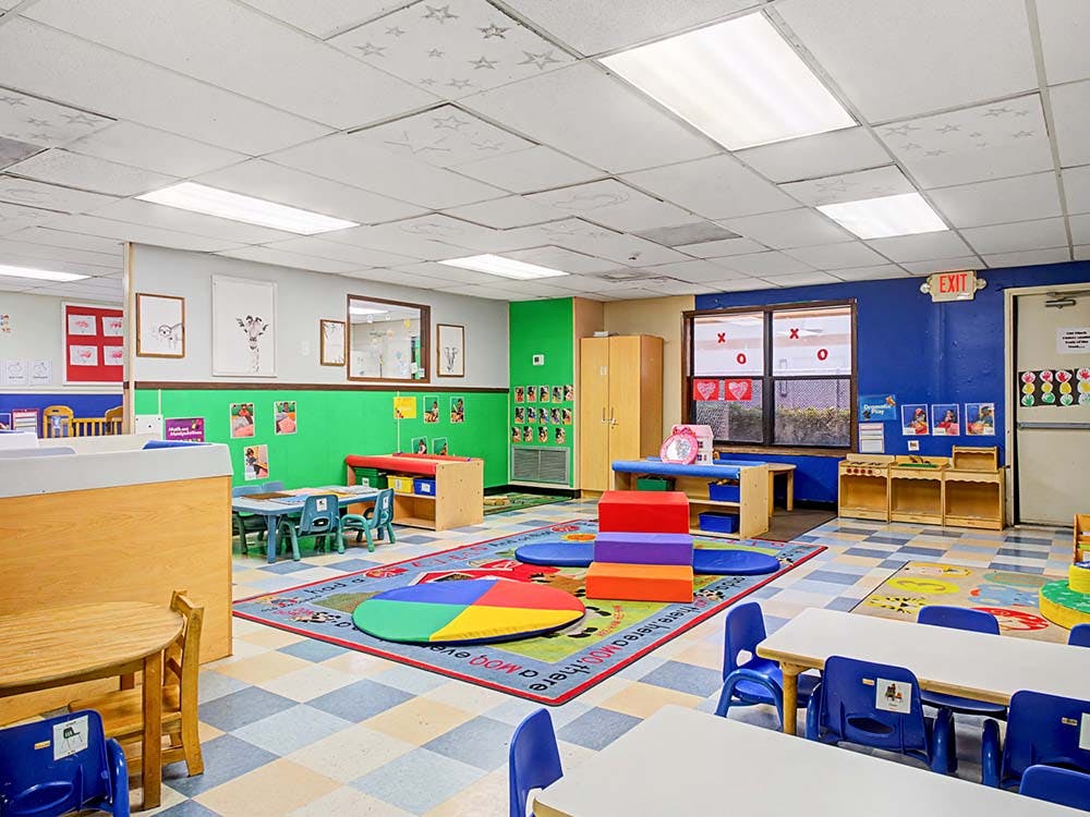 Empty colorful preschool classroom with tables, chairs, and play mats