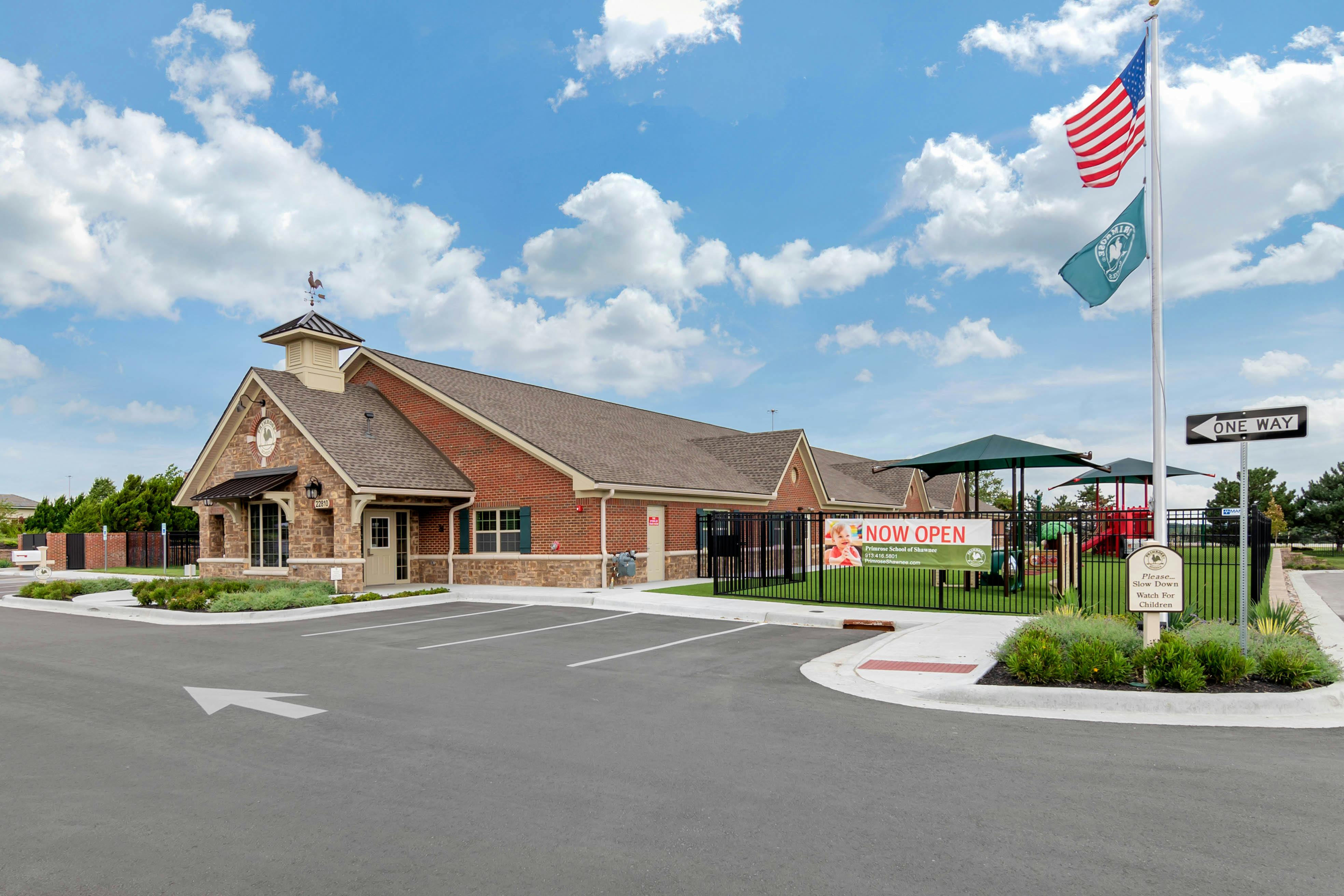 Brick building with a weather vane, "NOW OPEN" banner, and playground