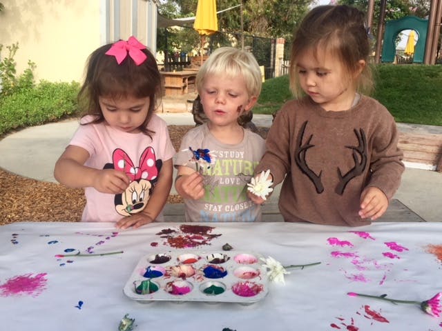 Three children painting with leaves and brushes at a table