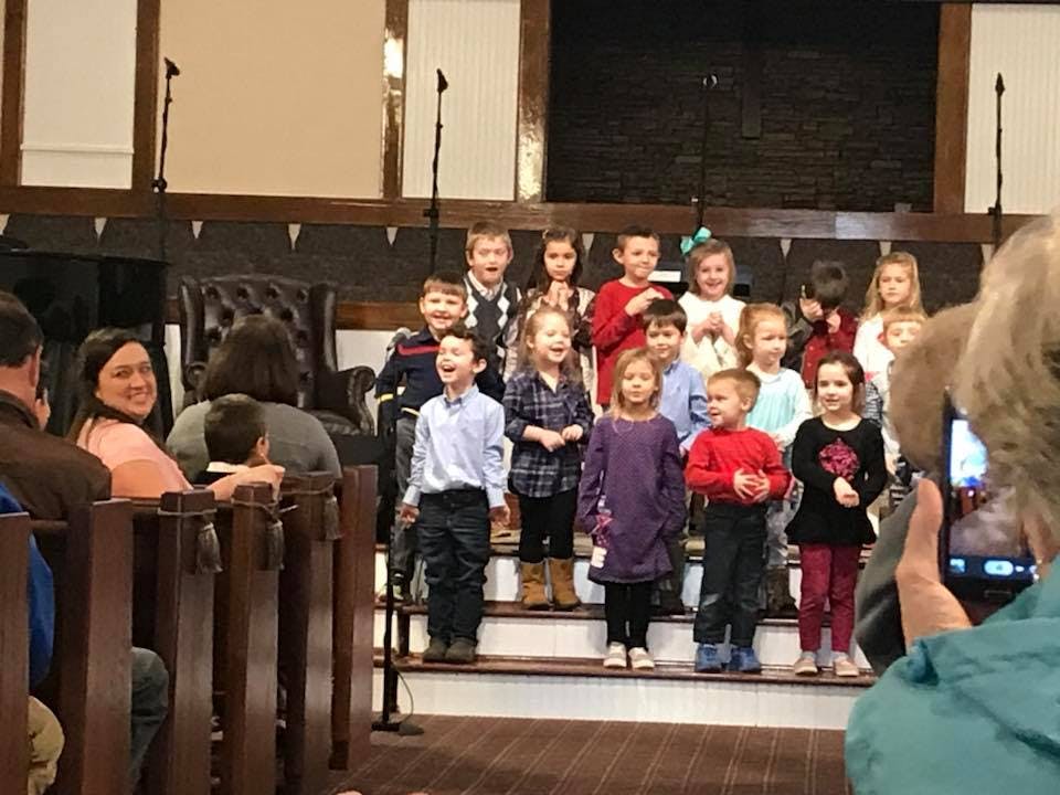 Children standing on steps, some smiling, with adults watching