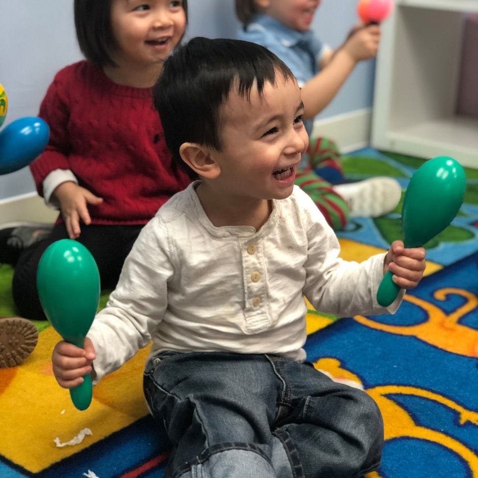 Child holding two green maracas, other children in background