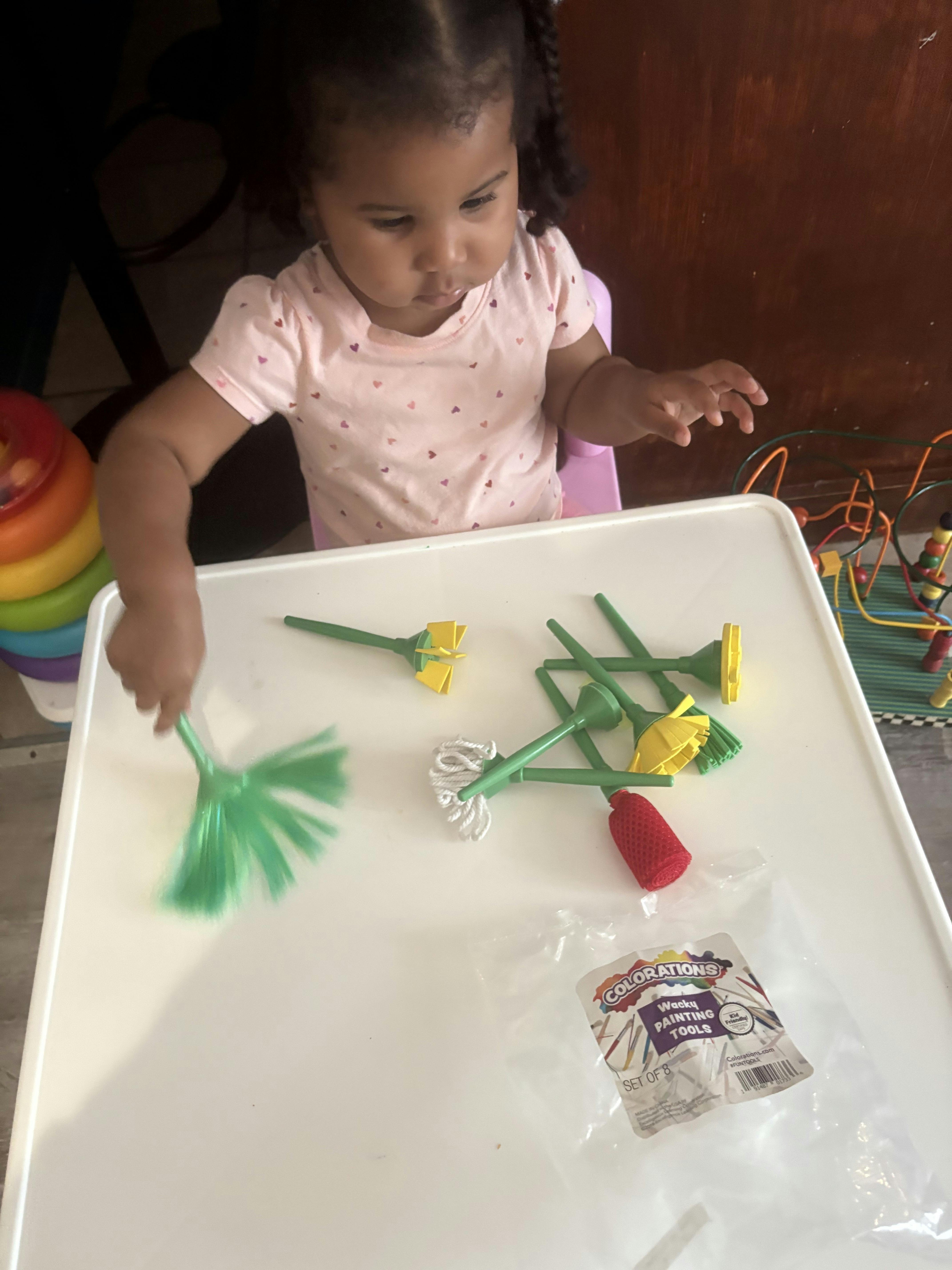 Child playing with toy cleaning tools on a white table