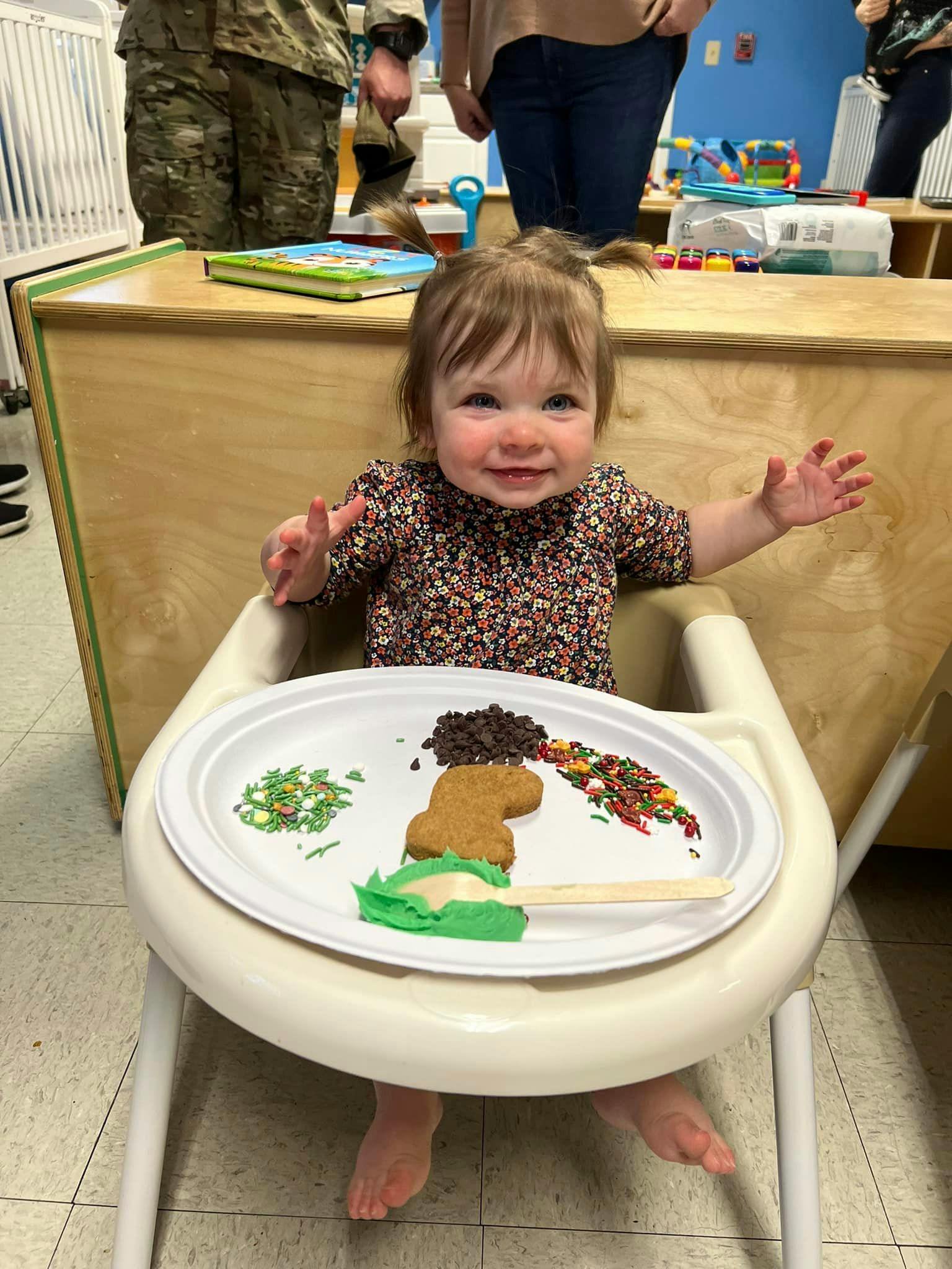 Child in a high chair with a plate of cookie decorating supplies