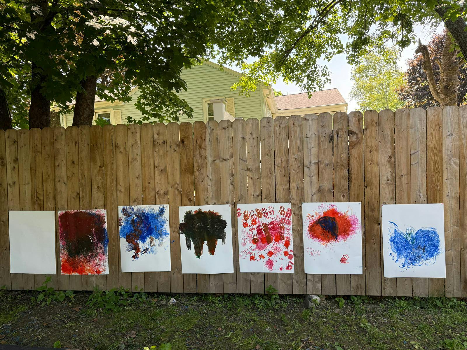 Child finger paintings hung on a wooden fence