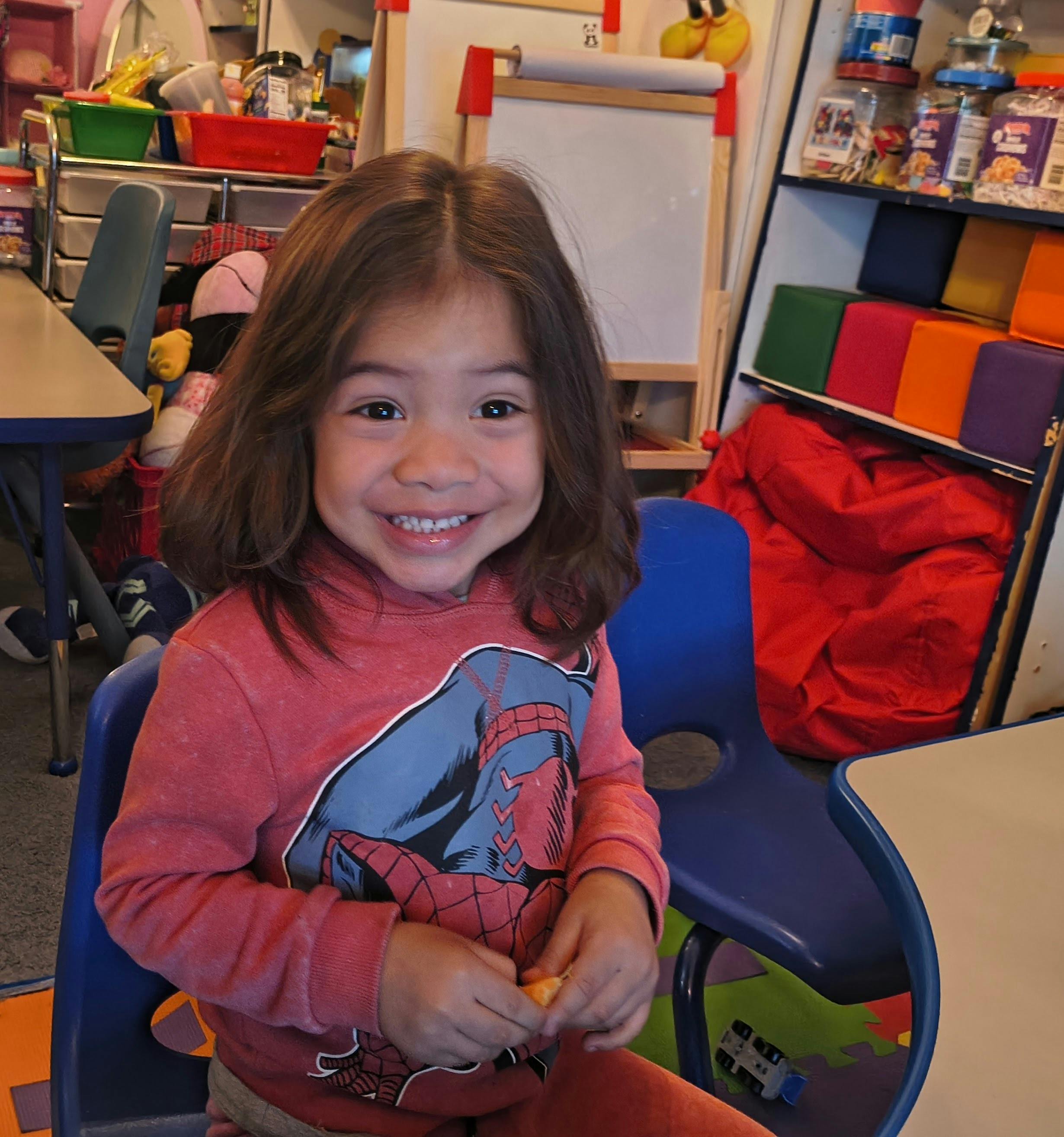Child in a Spider-Man sweatshirt peeling an orange in a classroom