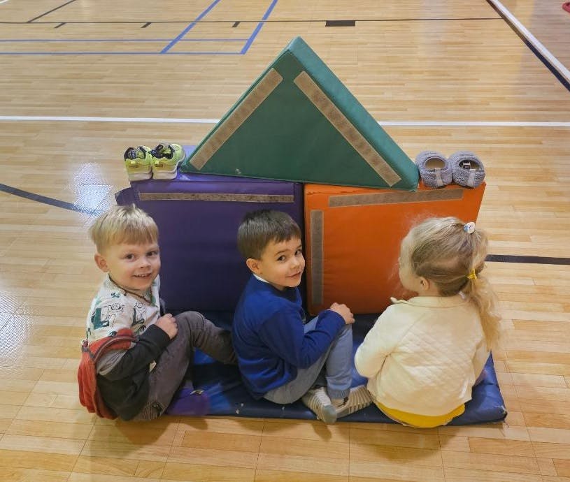 Three children sitting on a mat with colorful soft play blocks