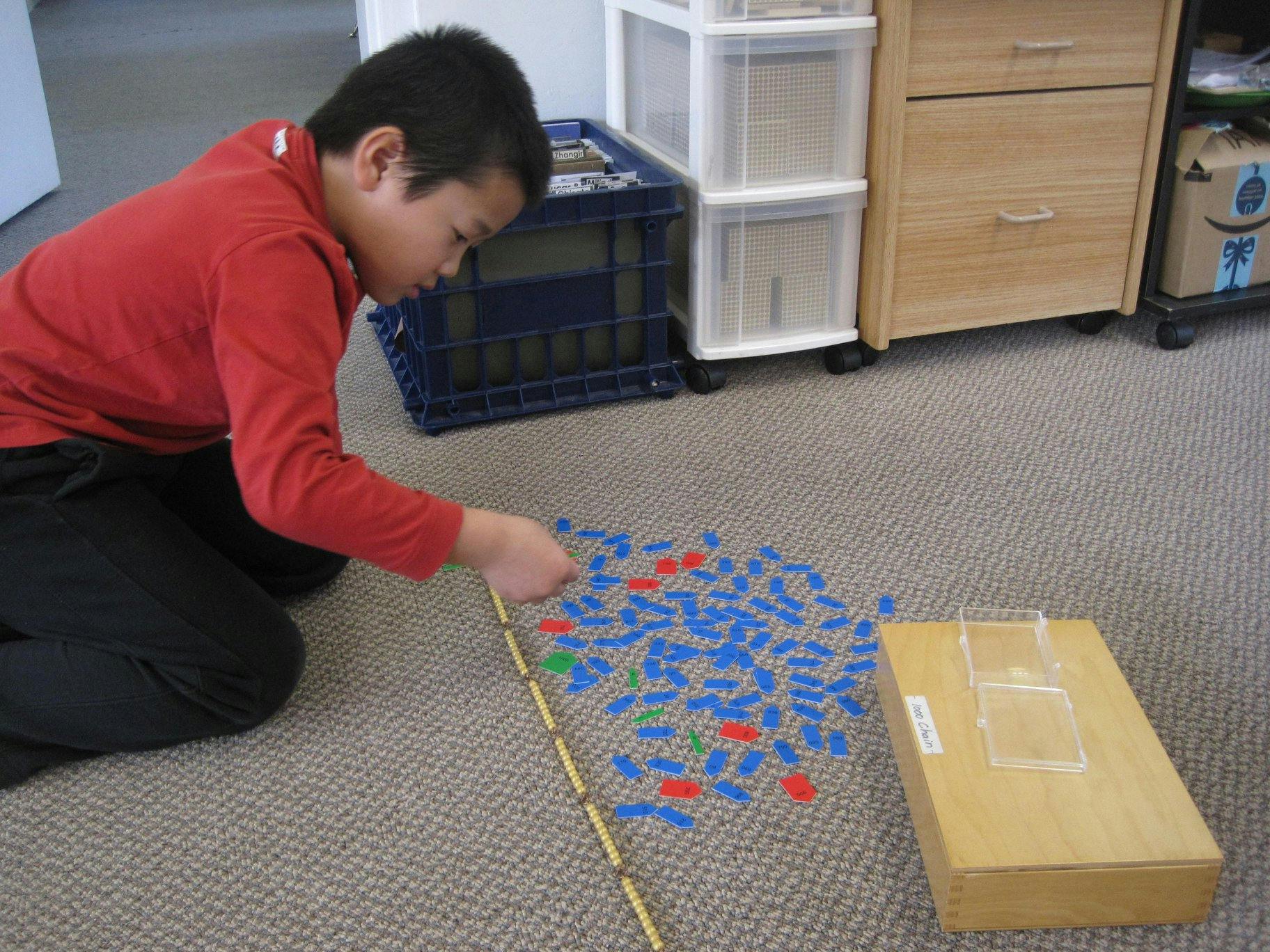 Child kneeling on floor, arranging small blue and red pieces with a stick