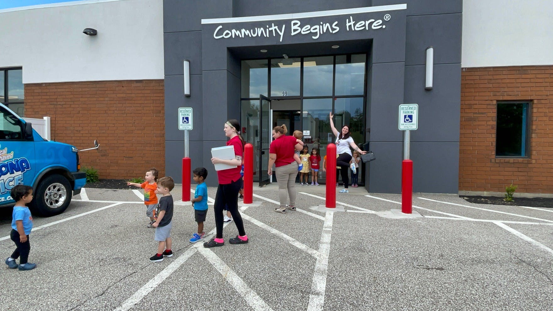 People and children outside a building with "Community Begins Here" above the entrance