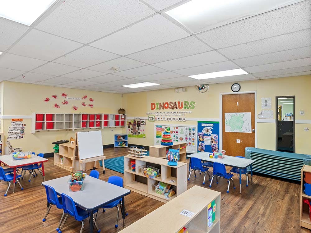An empty kindergarten classroom with small tables and chairs, and play items