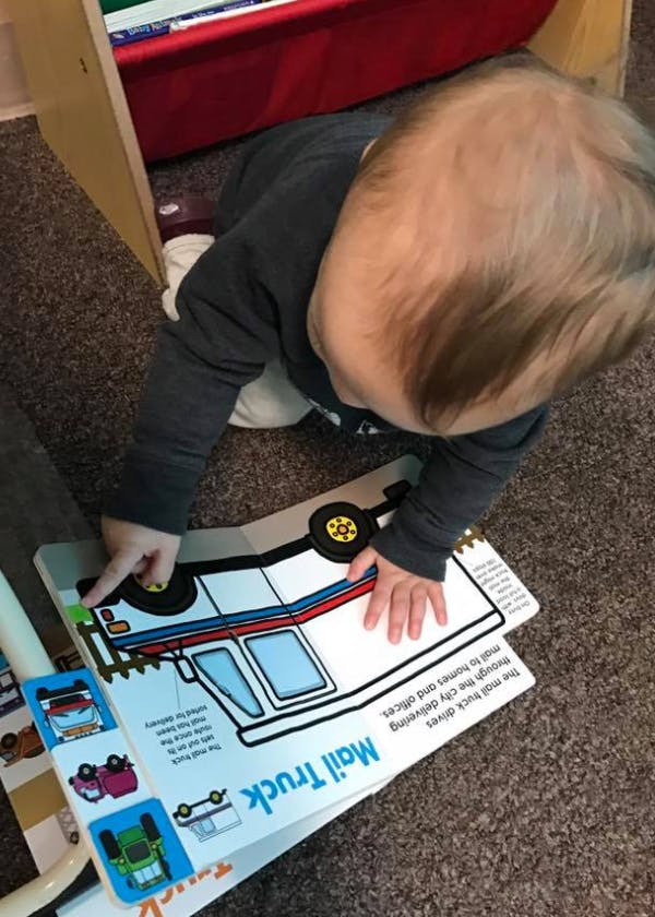 Child on floor looking at a book with a mail truck illustration