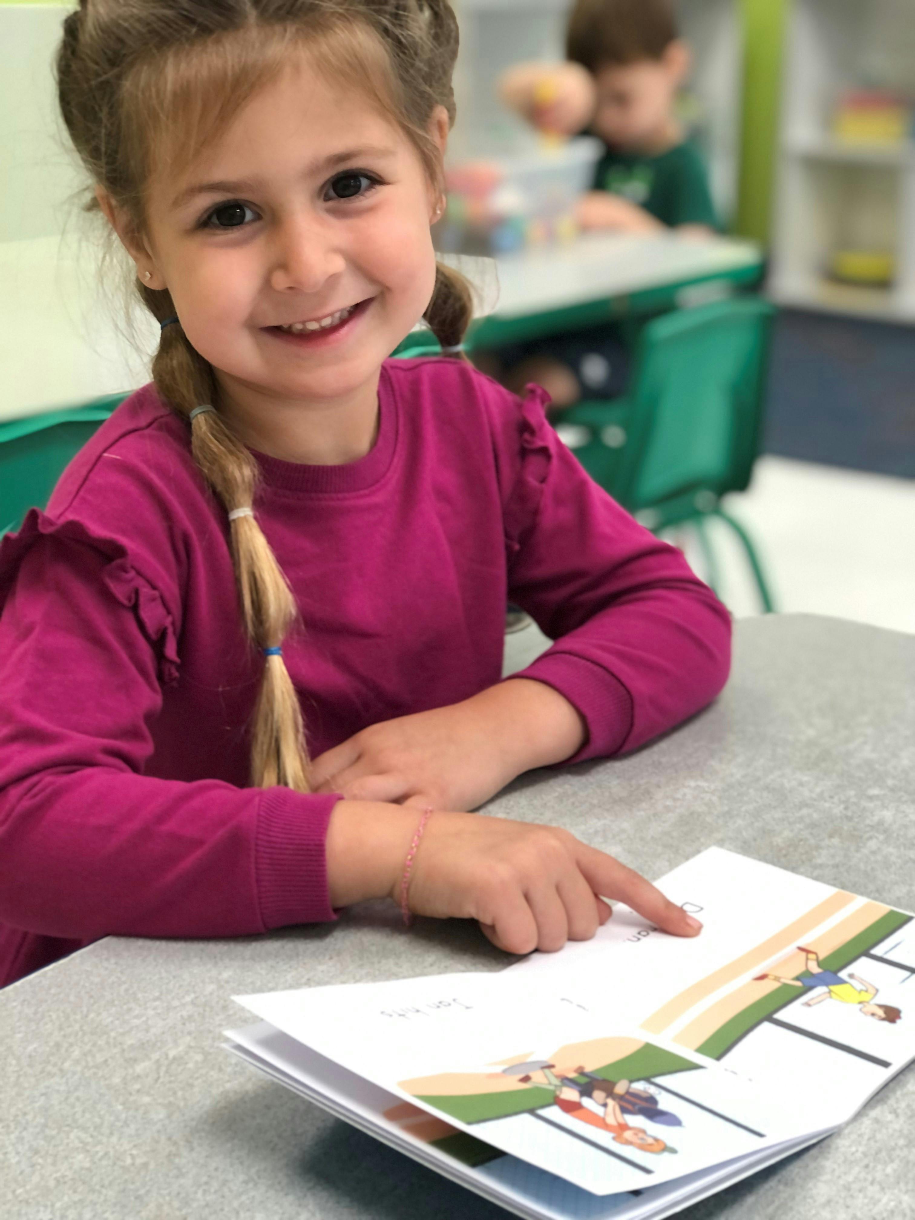 Child pointing at an open book on a desk in a classroom