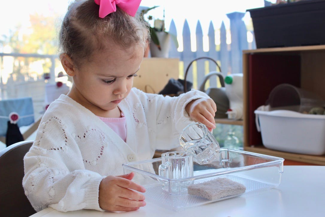Child pouring water from a small glass pitcher into a glass cup