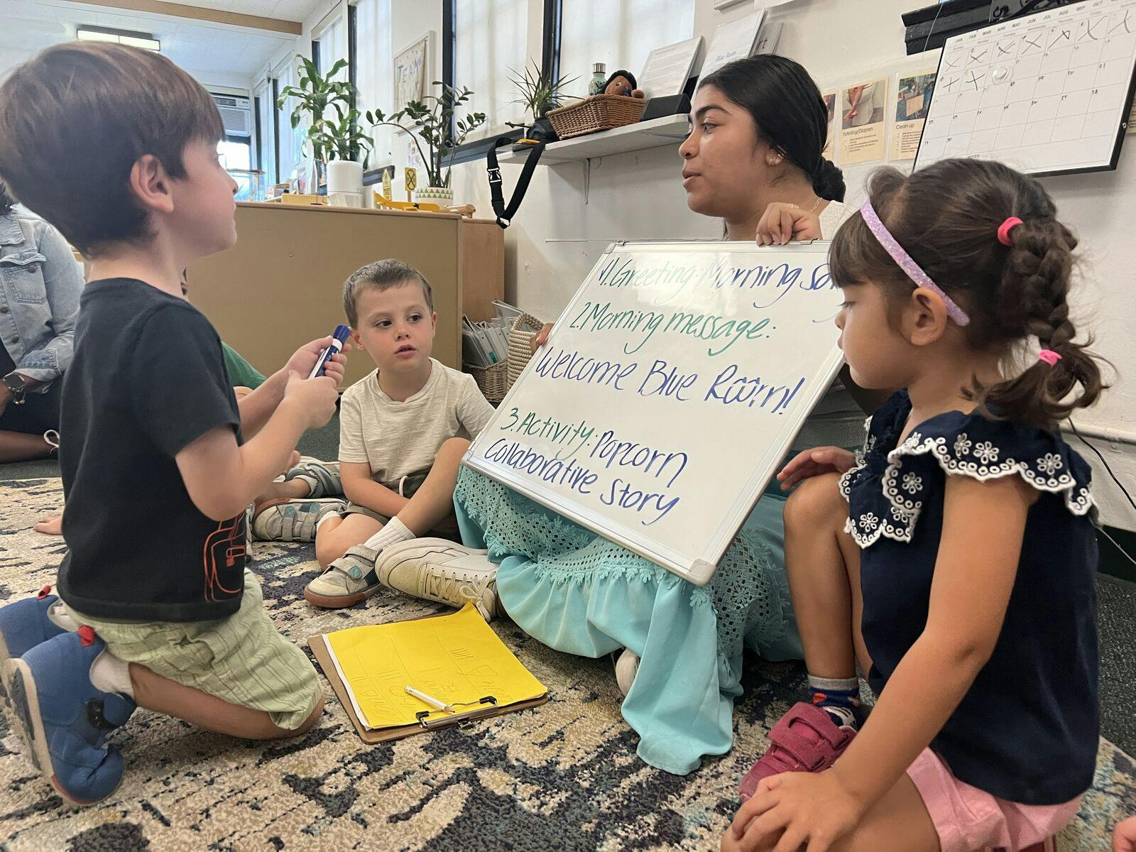 Adult holding a whiteboard with text, surrounded by three children in a classroom