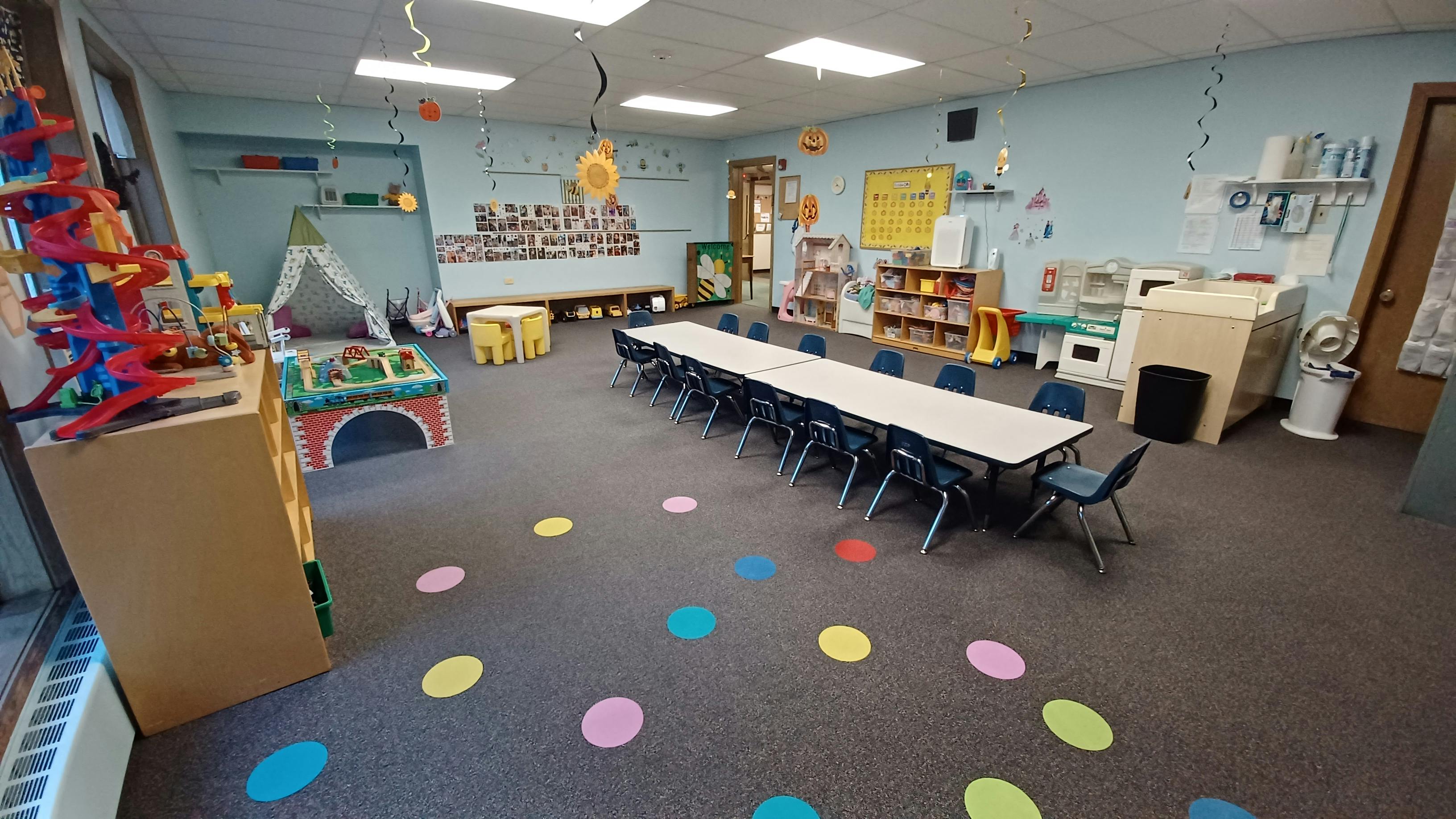 Classroom with long table and chairs, colorful floor dots, and play areas