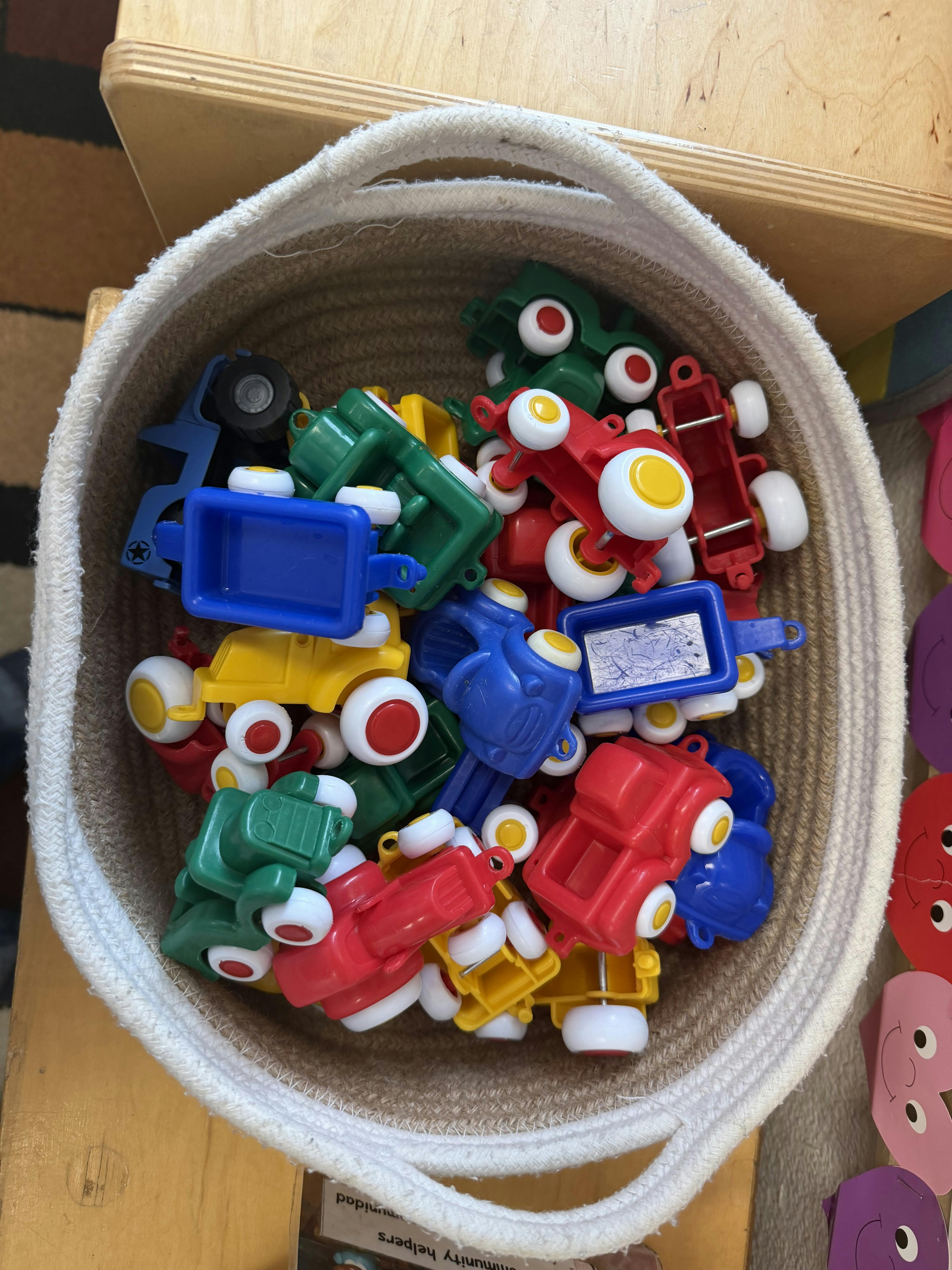 Top view of a woven basket filled with colorful toy plastic vehicles