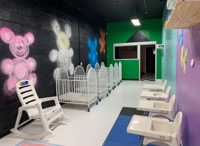 Row of white cribs and high chairs in a daycare room
