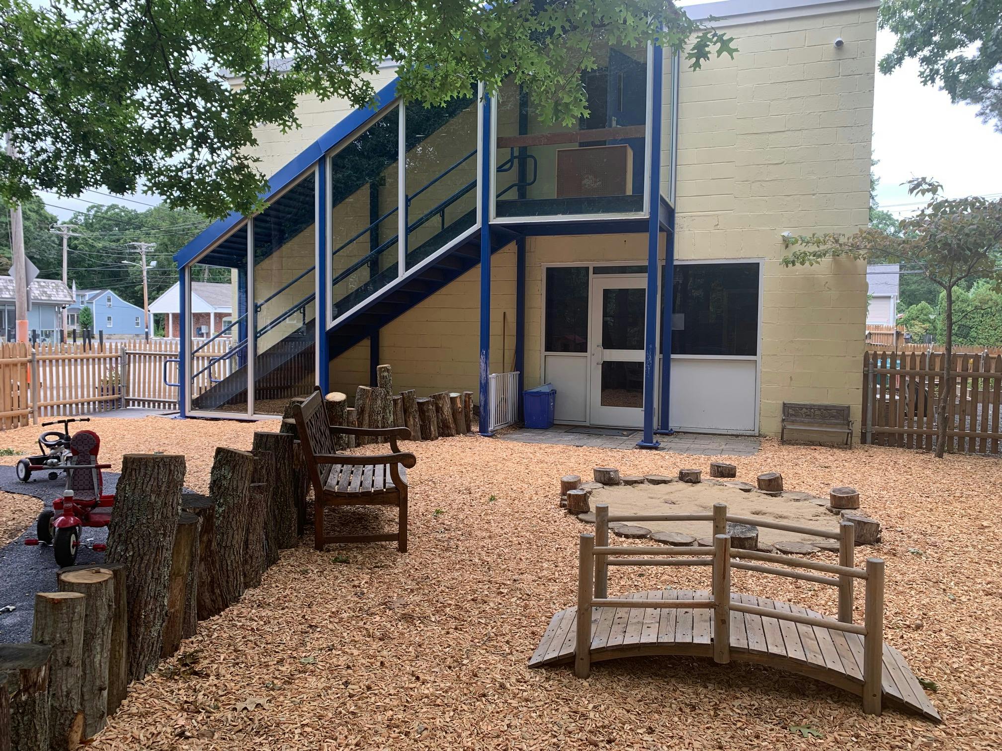 Outdoor playground with wood chips, small bridge, and building in background