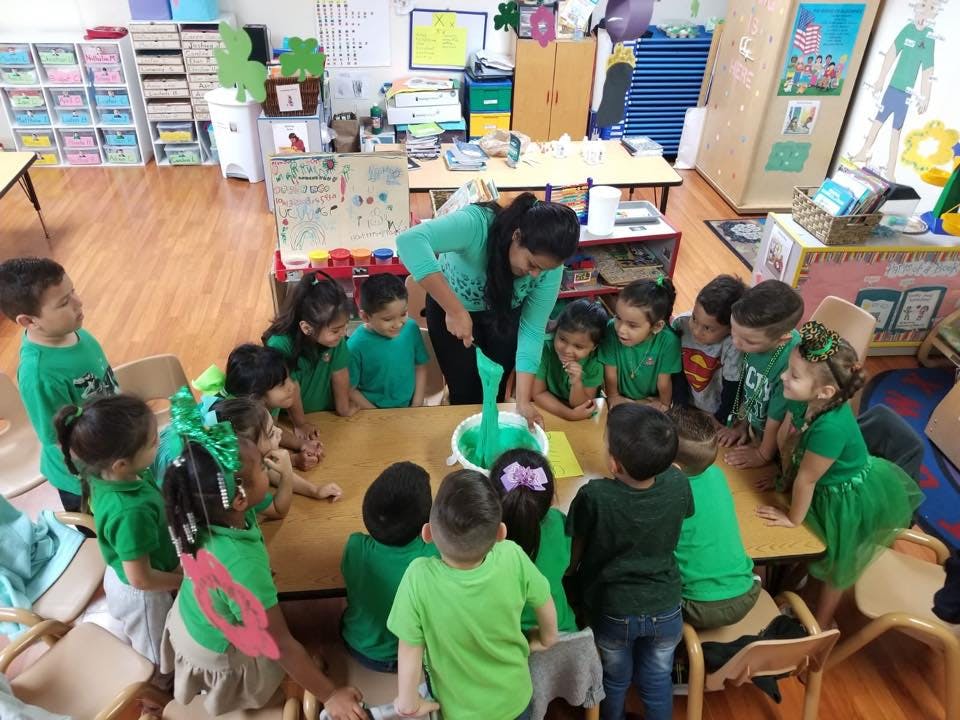 Adult and children in green shirts gathered around a table mixing a green substance