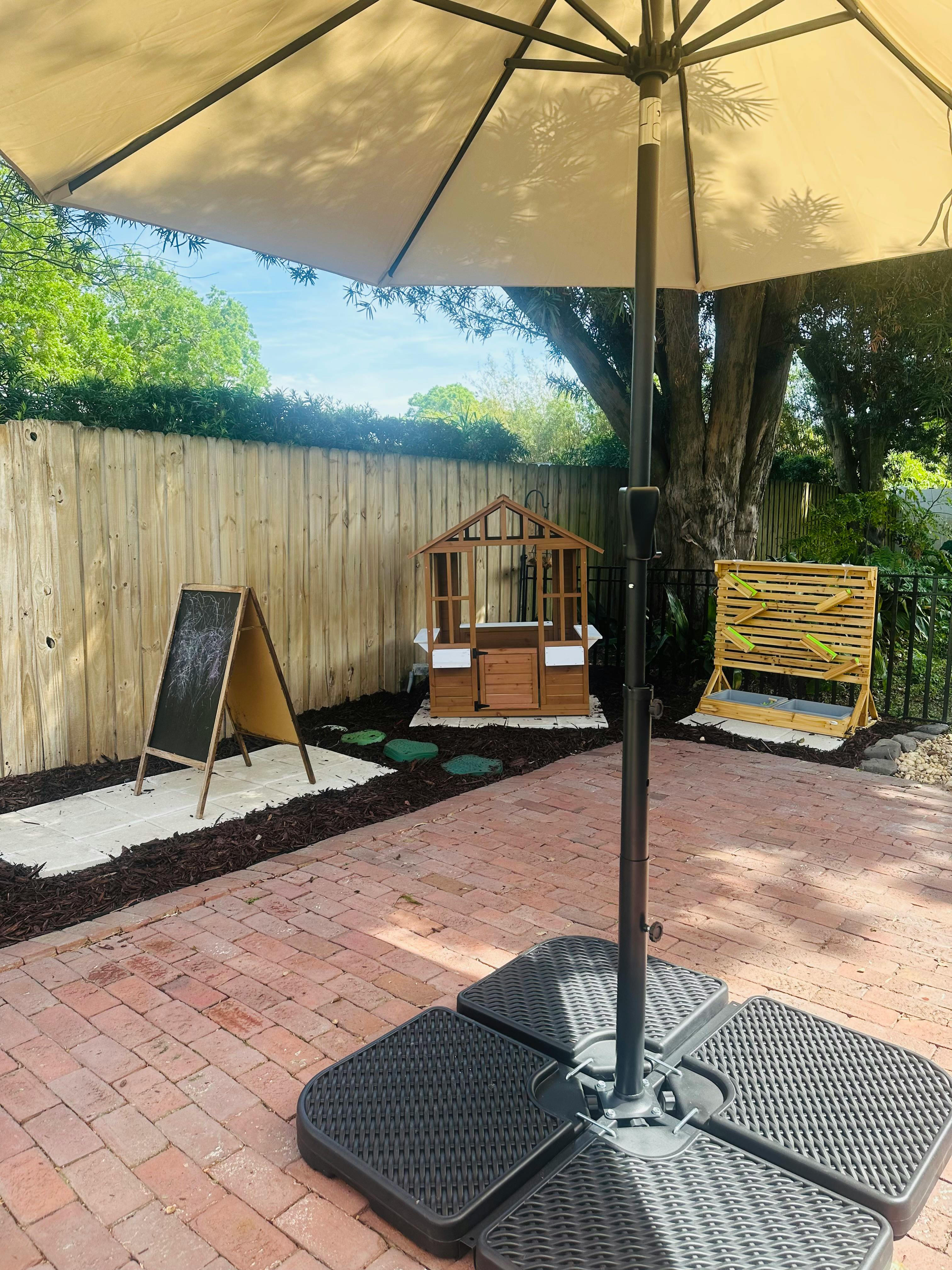Patio umbrella over a brick patio with a wooden fence and play structures