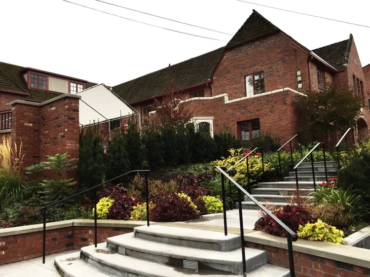 Brick building with a stepped concrete walkway and black railings through landscaping