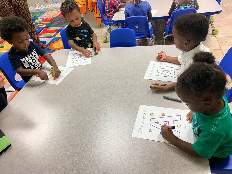 Four children coloring letter A worksheets at a table in a classroom
