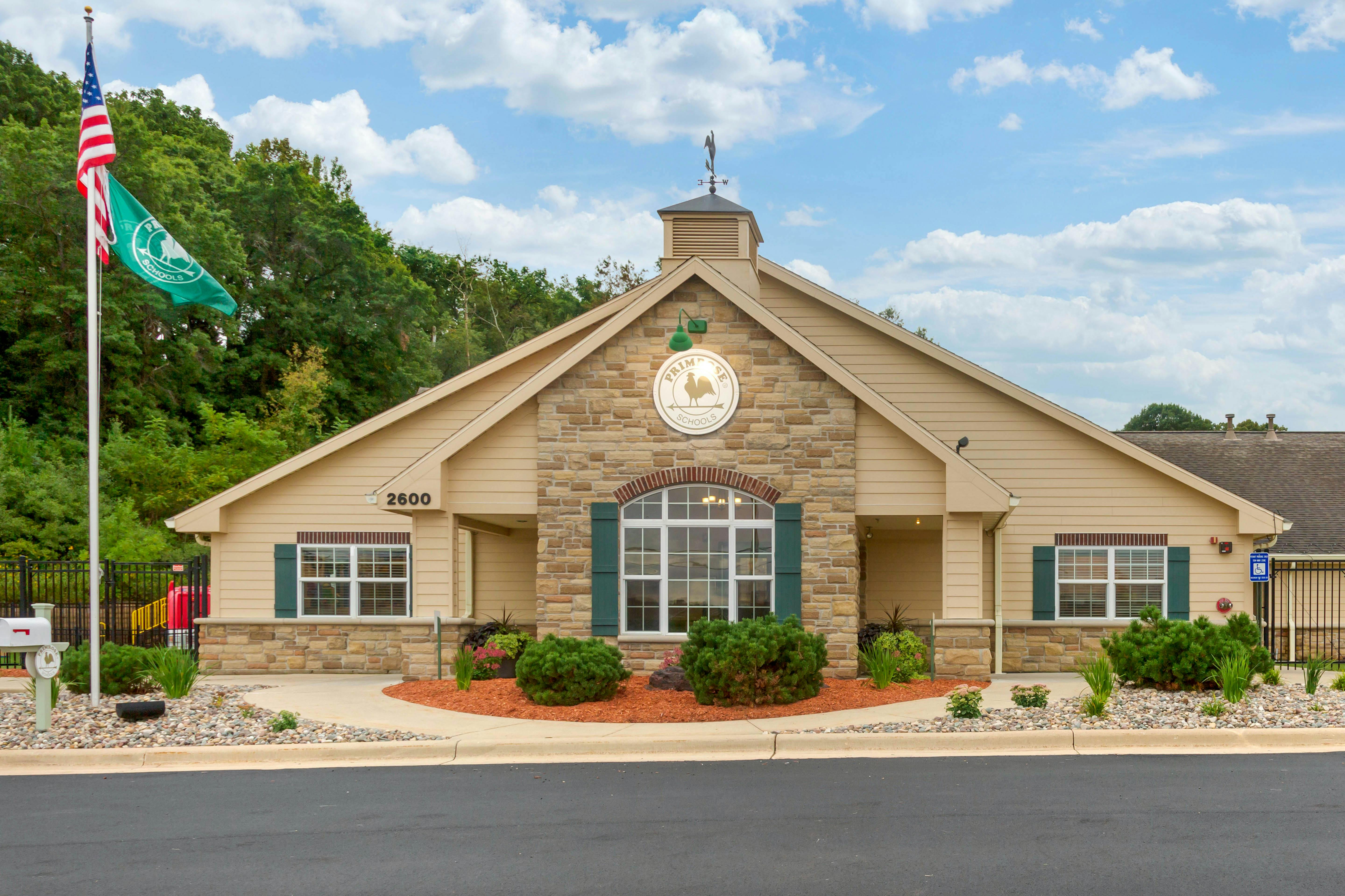 Exterior of a tan building with stone accents, green shutters, and a sign that reads "Primrose Schools"