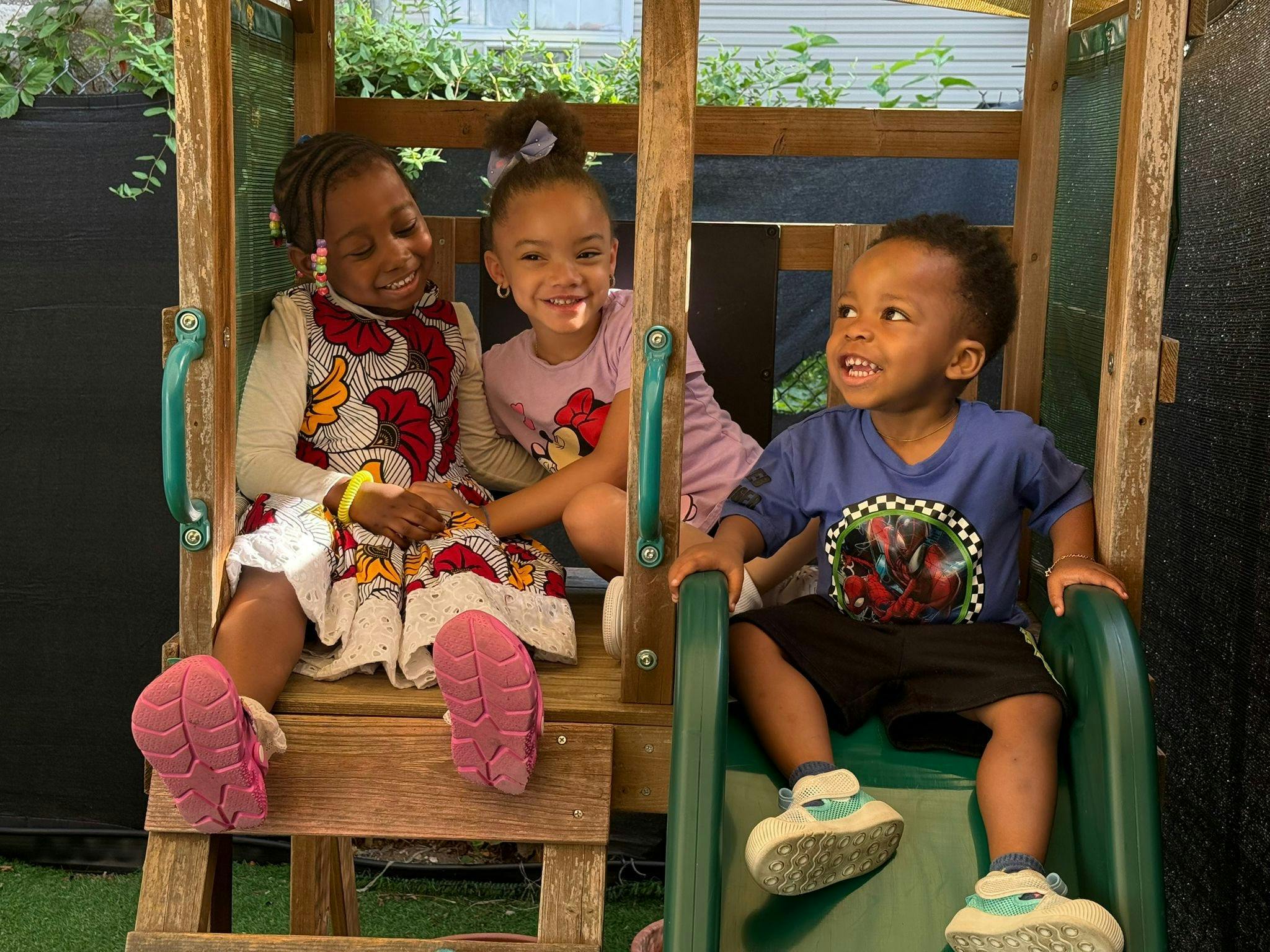 Three children on a playground structure, two sitting on a platform and one on a slide