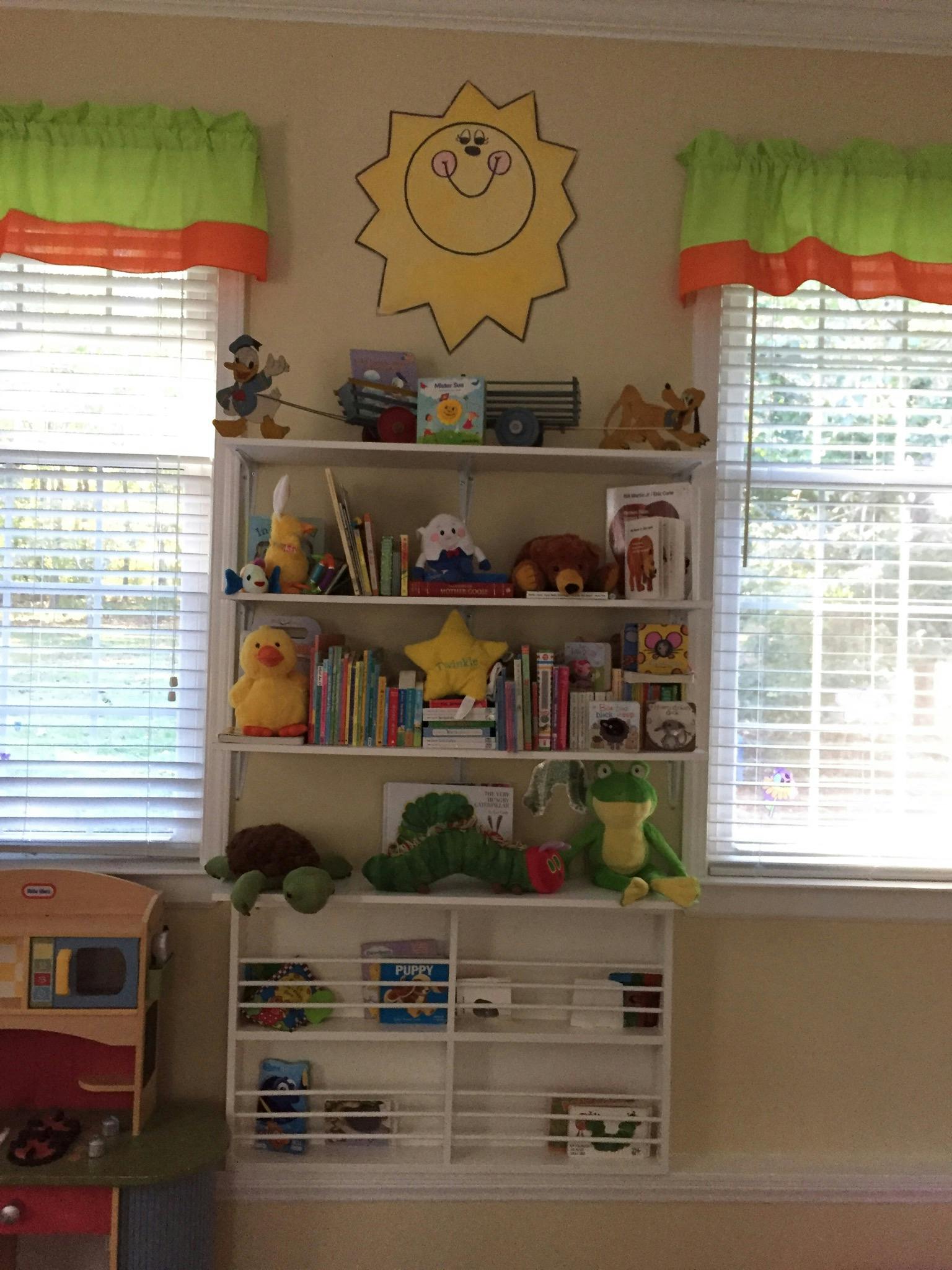Bookshelves filled with books and stuffed animals in a room with windows
