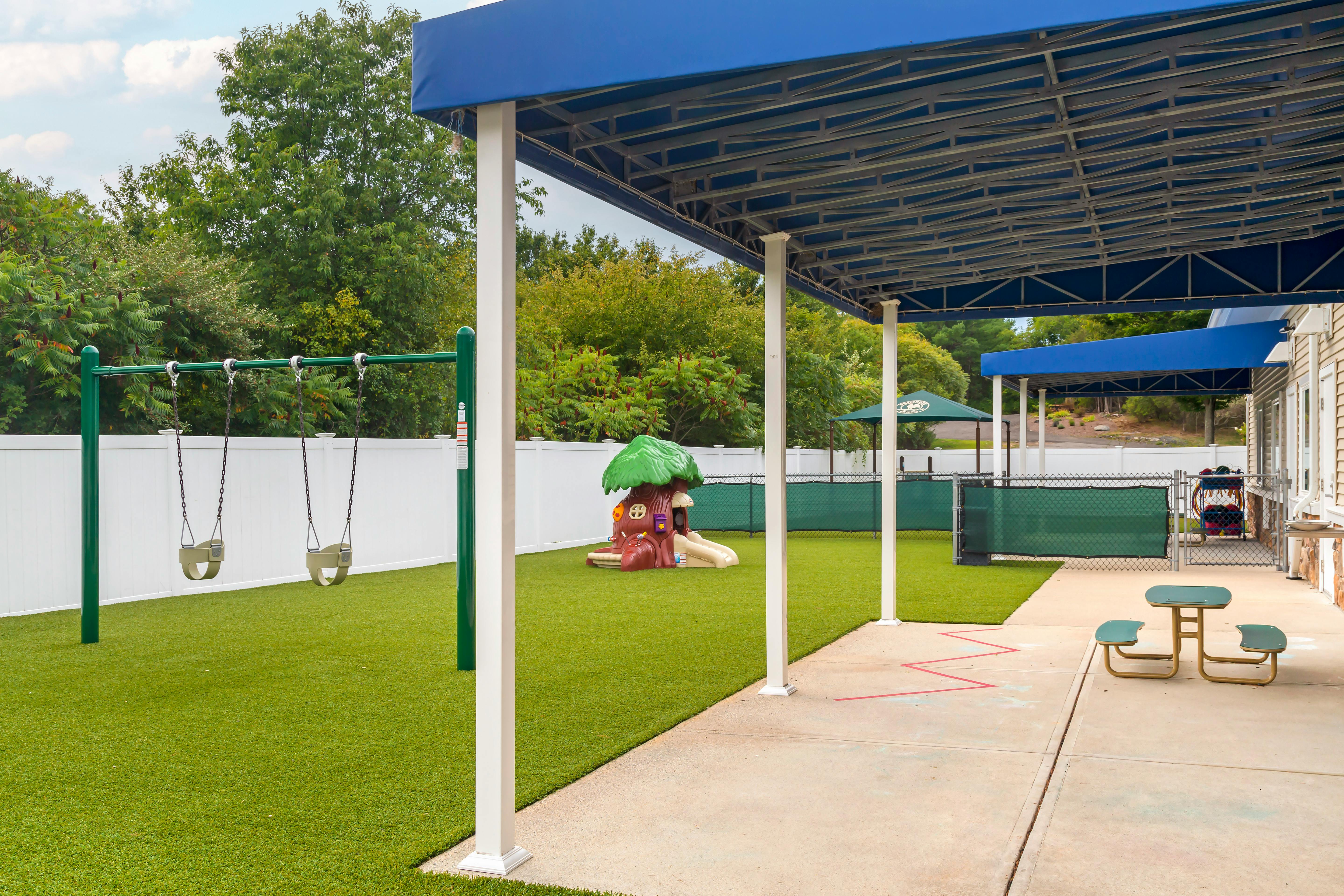 Outdoor playground with artificial turf, swings, and a small playhouse