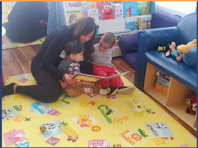 Person reading a book to two children on a play mat