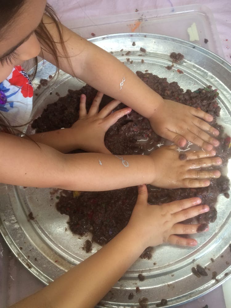 Children's hands pressing down on dark, textured material in a tray