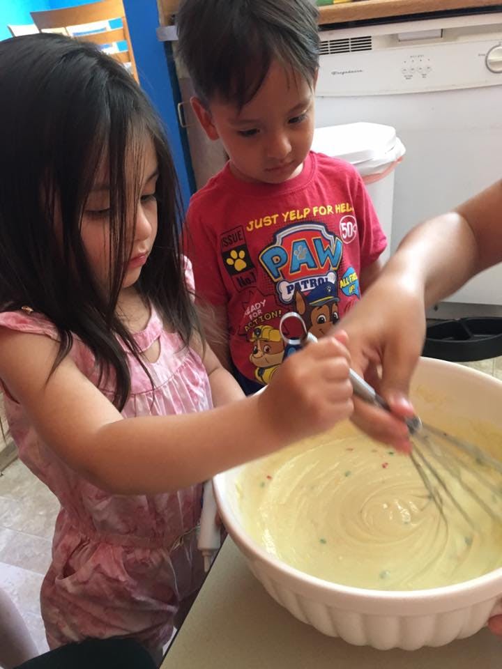 Two children watching a person whisking batter in a bowl
