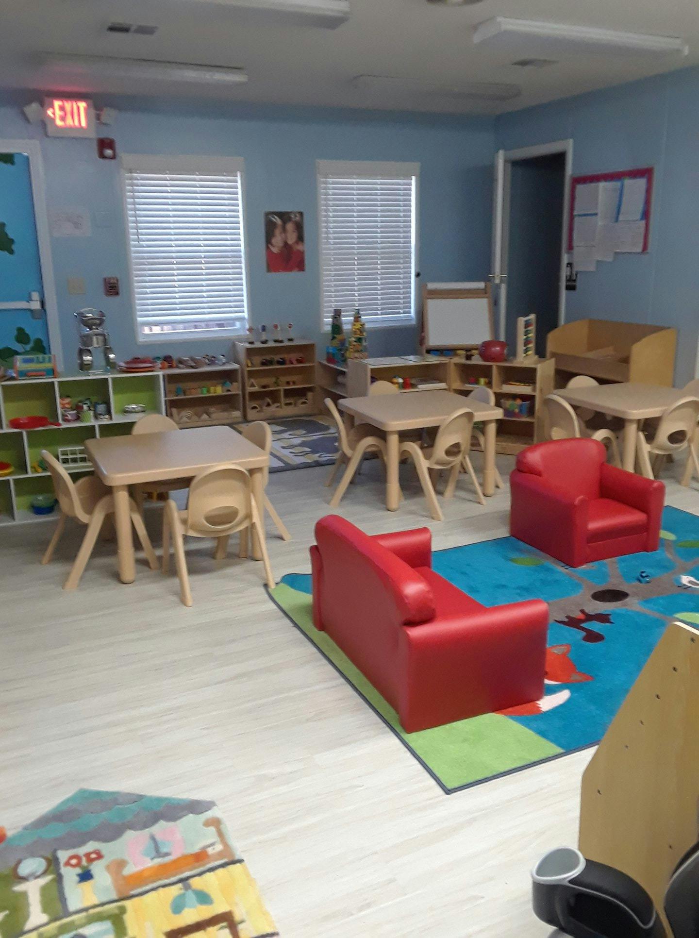 Classroom with small tables and chairs, red couches, and shelves with toys