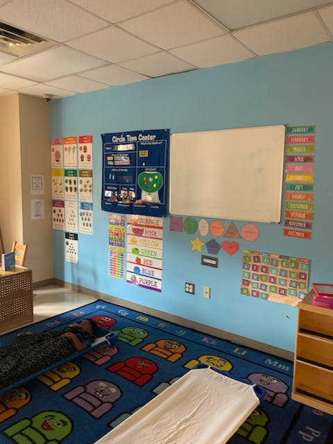 Classroom with blue walls, whiteboard, educational posters, and a colorful rug