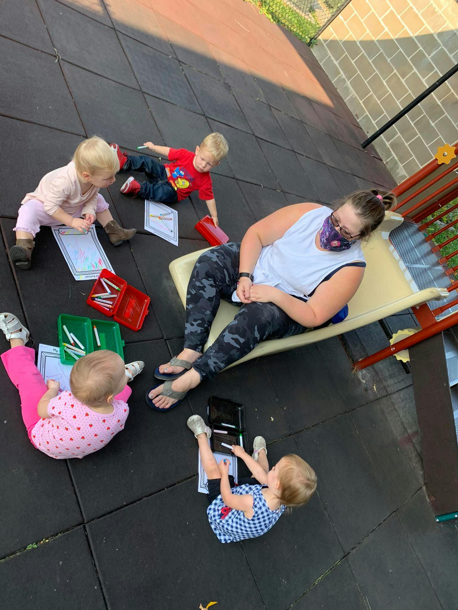 Adult and three children drawing on paper on the ground